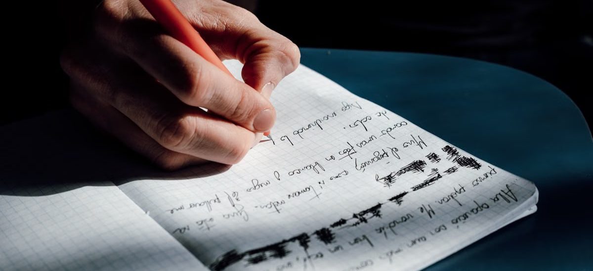 A person's hand writing in a notebook on a sunny day, showing detailed cursive notes.