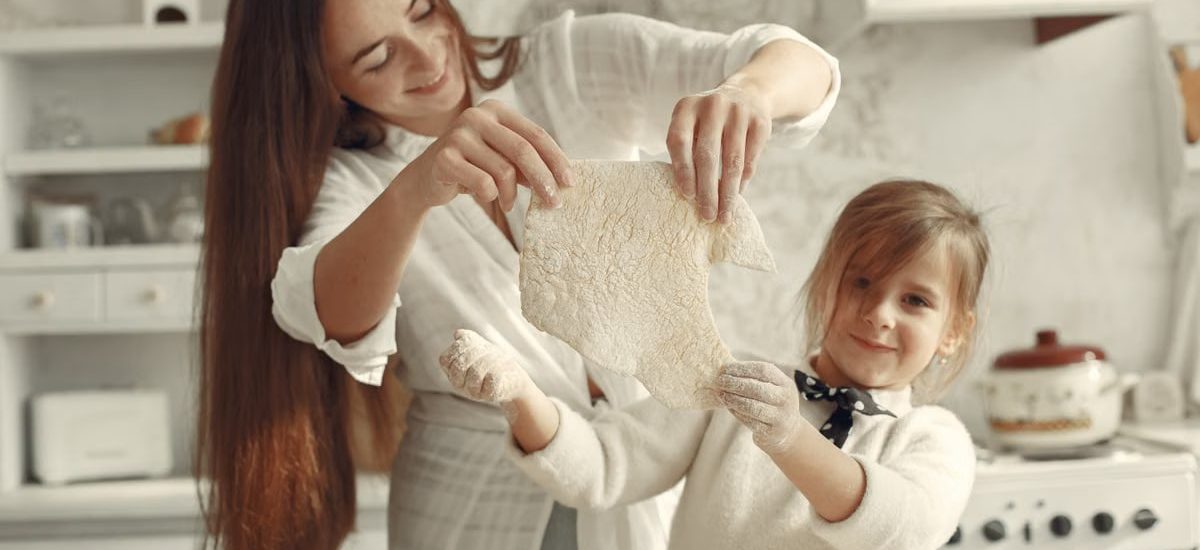 A mother and daughter joyfully preparing dough in a cozy kitchen setting.