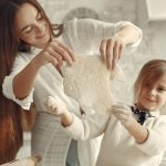 A mother and daughter joyfully preparing dough in a cozy kitchen setting.