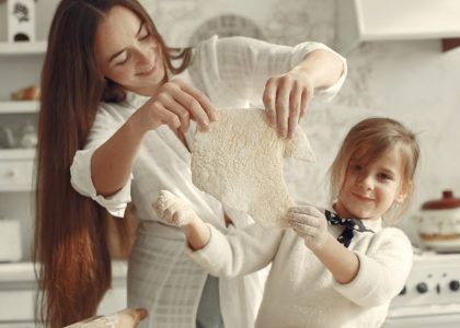 A mother and daughter joyfully preparing dough in a cozy kitchen setting.
